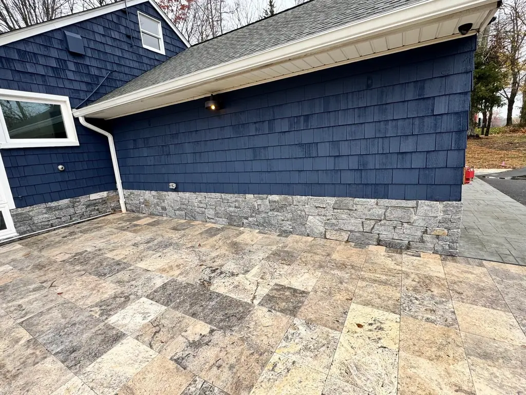 Natural stone veneer skirt on a shingled home, with a travertine paver patio